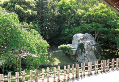 栄唱の間から望む花葉の池のふちに立つ大立石の写真
